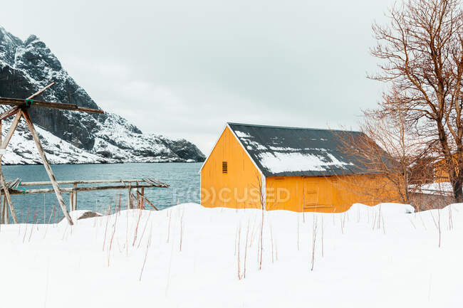 Желтая хижина, расположенная рядом с горным хребтом заснеженного морского побережья на Лофских островах, Норвегия — стоковое фото
