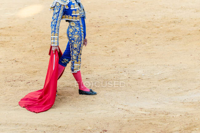 Crop of unrecognizable bullfighter in traditional costume holding estoc sword and capote while performing on bullfighting arena — Stock Photo