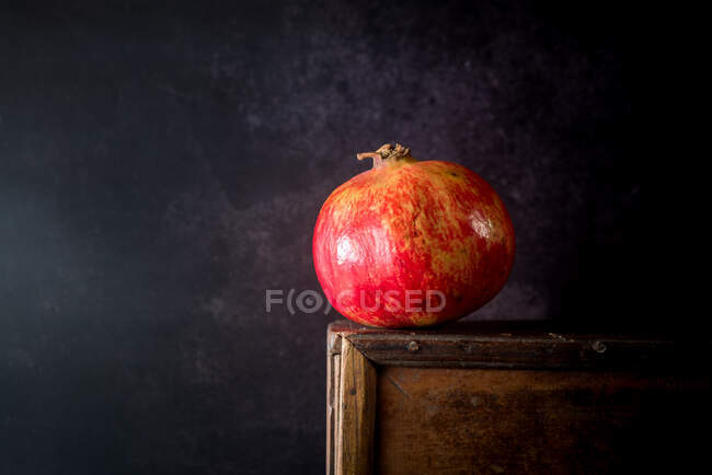Still life composition with bright red whole pomegranate fruit placed on wooden stand against black background — Stock Photo