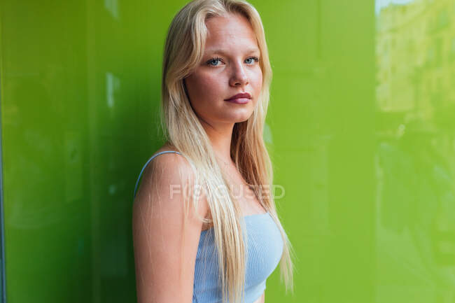 Seitenansicht einer Millennial-Frau mit blonden Haaren, die auf grünem Hintergrund in die Kamera zwinkert — Stockfoto