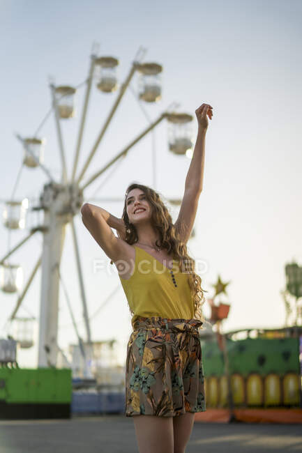 Baixo ângulo de fêmea encantada de pé com braços levantados no parque de diversões e desfrutando de fim de semana de verão — Fotografia de Stock
