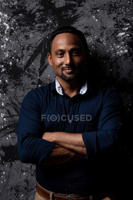 Happy stylish ethnic male standing on dark background looking at camera — Stock Photo