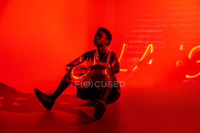 Schwarze Frau mit Basketballoutfit im Studio mit Farbgelen und Projektorlichtern auf orangefarbenem Hintergrund — Stockfoto