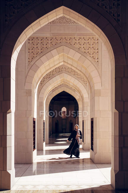 Full length of unrecognizable woman in traditional clothes walking through ornamental archway of Sultan Qaboos Grand Mosque in Muscat — Stock Photo
