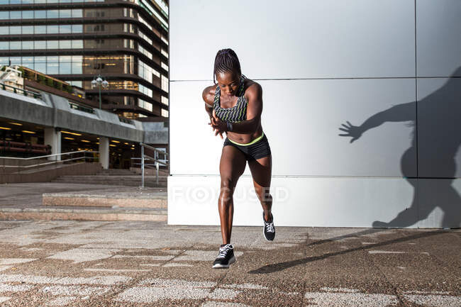 Seitenansicht einer afroamerikanischen Athletin, die vorwärts springt, während sie in der Nähe einer modernen Hauswand auf der Stadtstraße läuft — Stockfoto
