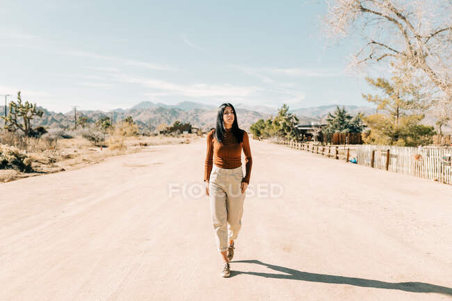 Full body of brunette walking down empty roadway in hot terrain of Joshua Tree National Park in California USA — Stock Photo