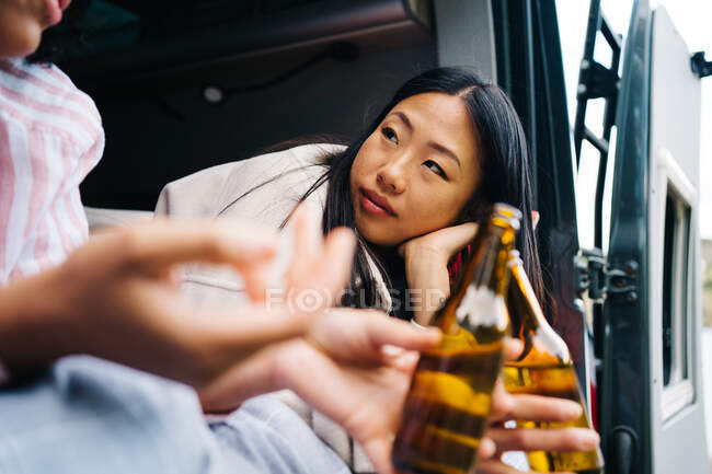 Молодые многорасовые женщины пьют пиво во время летнего путешествия в кемпере — стоковое фото