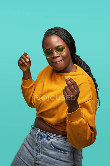 Femme afro-américaine joyeuse dans des lunettes de soleil jaunes à la mode dansant joyeusement sur fond bleu en studio — Photo de stock