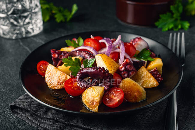 Ensalada sabrosa con pulpo y verduras y hierbas variadas en el plato en la mesa - foto de stock