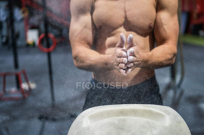 Atleta muscular irreconhecível espalhando giz nas mãos durante o exercício de levantamento de peso no ginásio — Fotografia de Stock