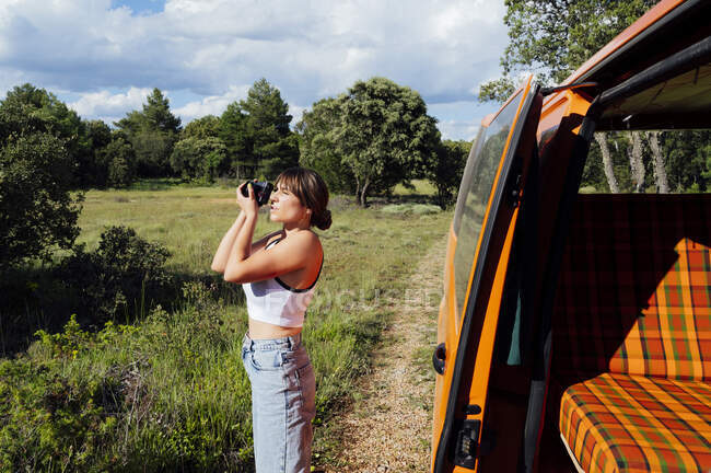 Encantado viajando fotógrafo feminino tirar fotos na câmera profissional durante as férias na floresta — Fotografia de Stock