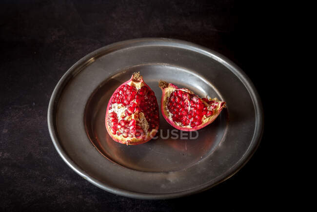 Von oben süße reife Granatapfelstücke auf Teller auf schwarzem Tisch serviert — Stockfoto