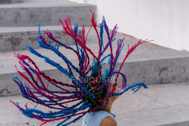 Side view of ethnic child with flying colorful braids standing near concrete staircase — Stock Photo