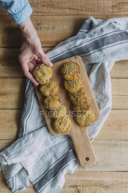 Вид на анонимного человека, берущего вкусный сладкий картофельный фалафель из раскроя доски над салфеткой и деревянным столом на кухне — стоковое фото