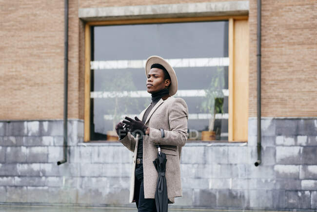 Retrato de hombre negro elegante con abrigo gris en la calle mirando hacia otro lado - foto de stock