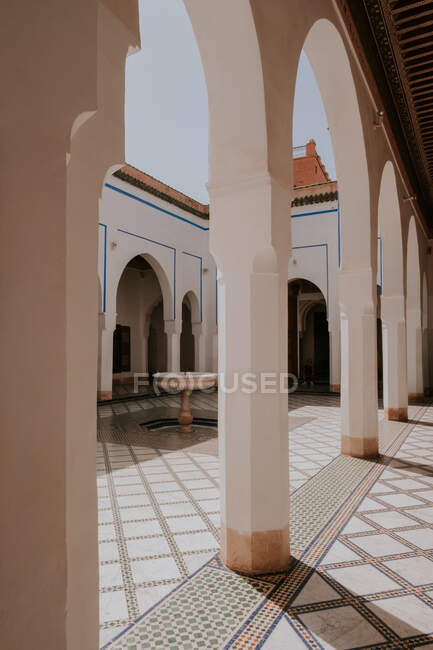 Columnas y arcos que decoran el patio de mármol del edificio islámico con fuente en el día soleado en Marrakech, Marruecos - foto de stock