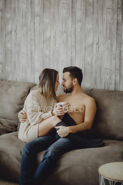 Счастливые мужчина и женщина с кружкой горячего напитка улыбаясь и глядя друг на друга, проводя время дома утром — стоковое фото