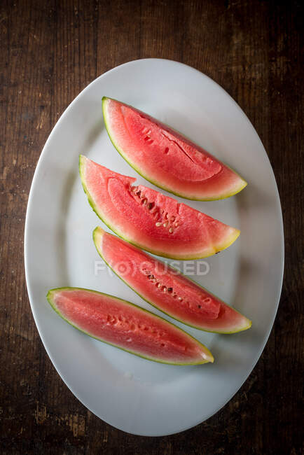 Alto ângulo de fatias de melancia doce madura na placa cerâmica colocada na mesa de madeira no fundo escuro — Fotografia de Stock