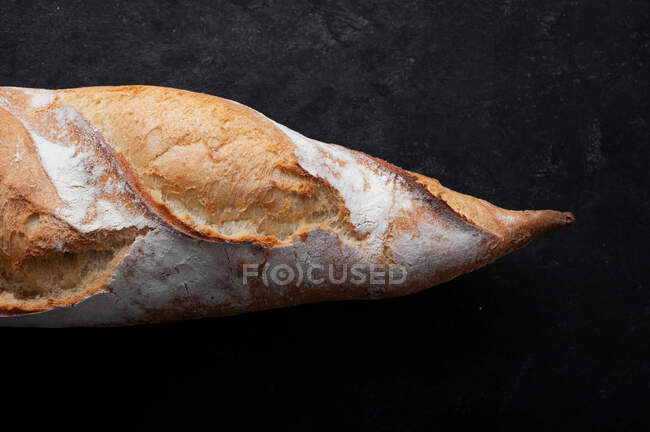 Appetizing freshly baked baguette with crispy crust placed on table against black background — Stock Photo