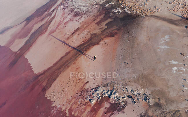 Von oben Luftaufnahme eines einsamen Abenteurers, der unwegsames, hügeliges, trockenes Gelände mit rosafarbener Oberfläche durchquert — Stockfoto