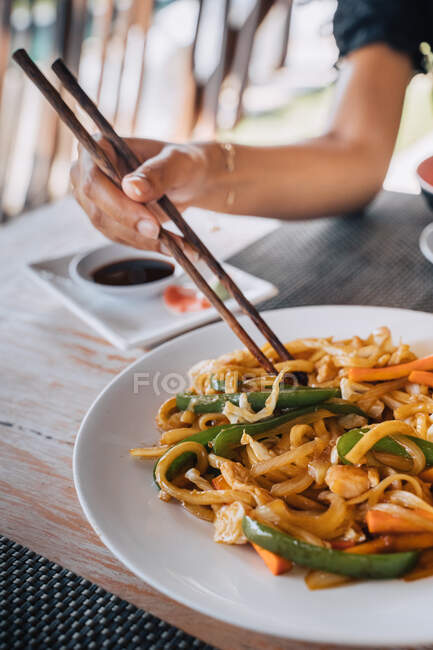 Анонимная туристка с вкусной пастой между палочками для еды над столом с соевым соусом и маринованными ломтиками имбиря на открытом воздухе — стоковое фото