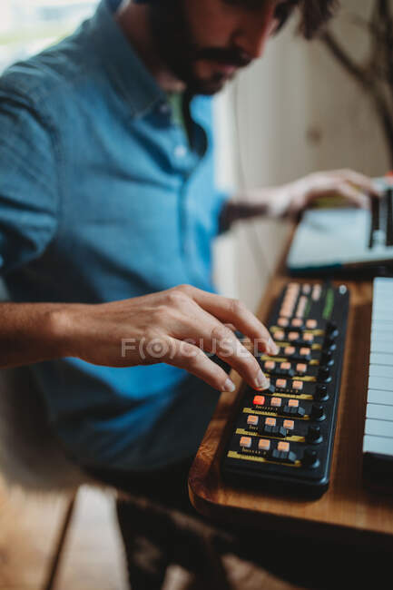 Side view of young unrecognizable man in headphones using synthesizer and laptop at table at home — Stock Photo