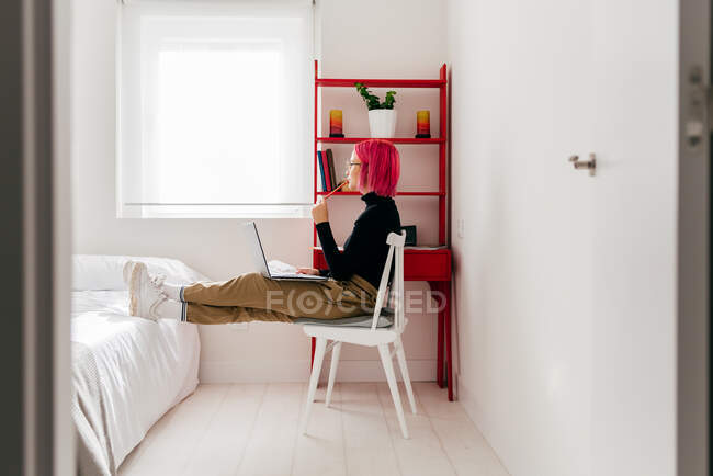 Вид збоку на зосереджених молодих фрілансерів у повсякденному одязі, що сидить на стільці та використовує ноутбук під час роботи над проектом у світлій сучасній квартирі — стокове фото