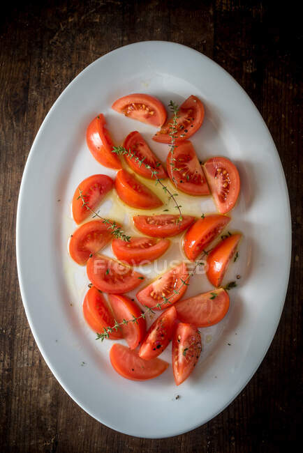 Vista superior de apetitosas piezas de tomate con hierbas verdes servidas en plato sobre mesa de madera - foto de stock