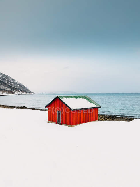 Cabaña roja situada en la costa blanca y nevada del mar contra el cielo azul sin nubes en las Islas Lofoten, Noruega - foto de stock