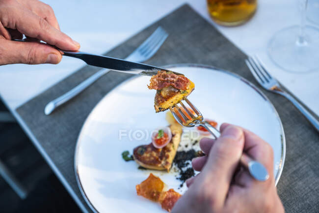 Hands holding cutlery on well garnished fried goose liver dish at outdoor high cuisine restaurant — Stock Photo