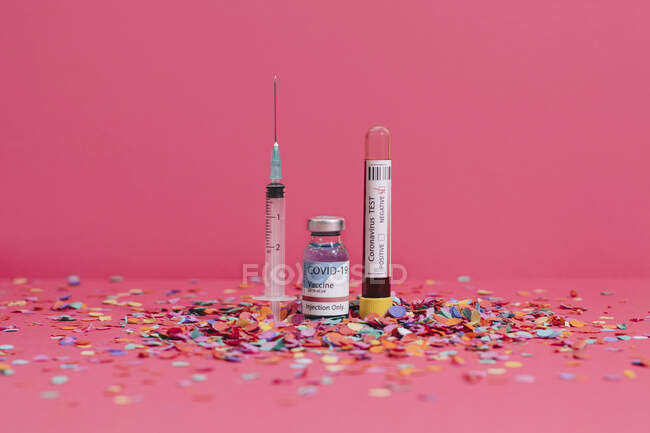Флакон коронавирусной вакцины рядом с анализом крови и шприц на розовом фоне, покрытый конфетти — стоковое фото