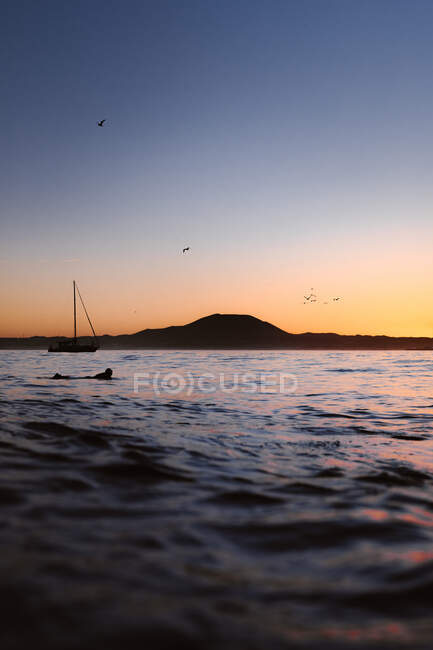 Anonimo maschio surfista silhouette su tavola da surf praticare sport estremi sul mare onda sotto il cielo al tramonto — Foto stock