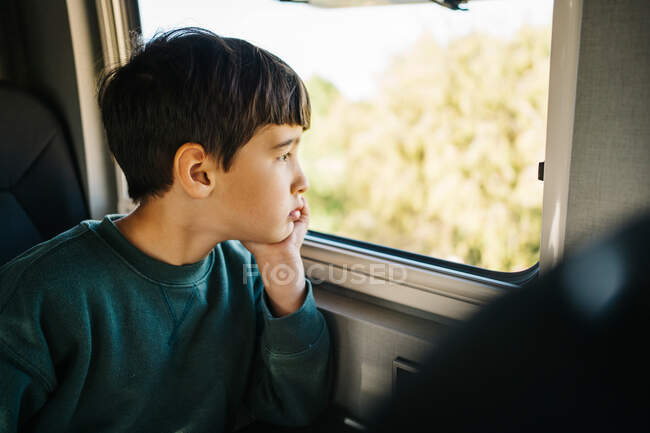 Vue latérale d'un petit garçon regardant par la fenêtre d'un camping-car — Photo de stock