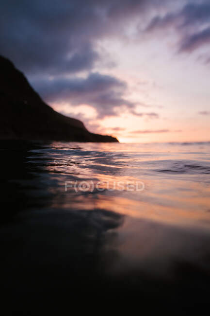 Agitant la mer bleue roulant sur le bord de la mer près d'une montagne lointaine au coucher du soleil — Photo de stock