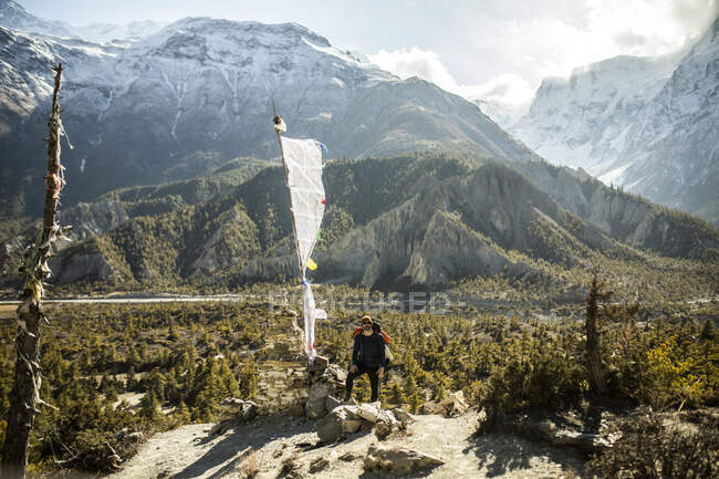 Männlicher Wanderer steht an einem sonnigen Tag in Nepal in der Nähe der weißen Flagge im Gebirgstal im Himalaya — Stockfoto