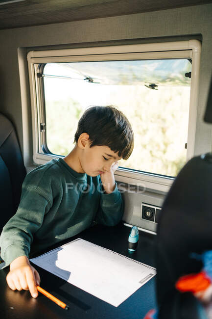 Kleiner Junge sitzt im Wohnmobil, während er seine Hausaufgaben macht — Stockfoto