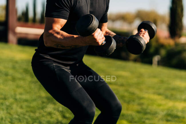 Crop male athlete in sportswear working out with dumbbell while looking forward under light sky — Stock Photo
