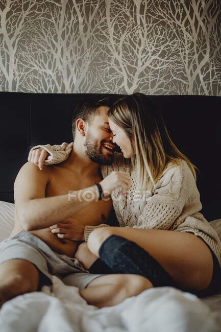 Cheerful young man and woman smiling and cuddling while lying on comfortable bed at home together — Stock Photo