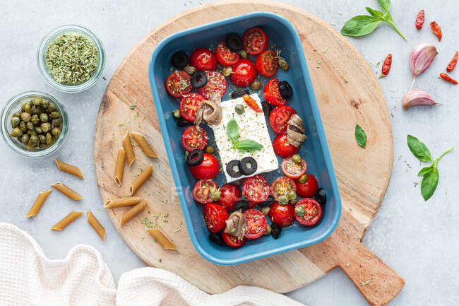 Top view of ripe cherry tomatoes with black olive slices and feta cheese in baking dish near uncooked penne — Stock Photo