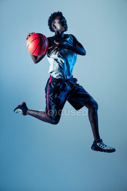 Черная женщина в баскетбольной форме в студии с помощью цветных гелей и прожекторов — стоковое фото