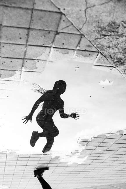 Crop leg and reflection in paddle of water of anonymous female athlete running on city street during outdoor workout — Stock Photo