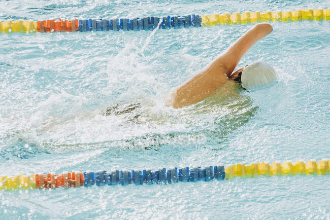 From above back view of unrecognizable paralympic sportsman in goggles and cap without hand swimming crawl style in pool between lanes — Stock Photo