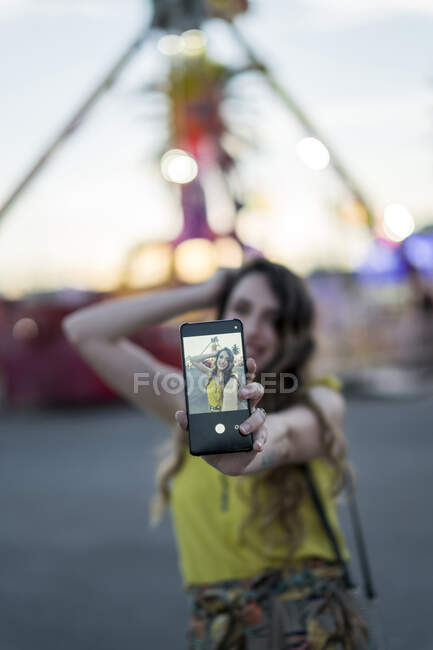 Contenuto femminile scattare autoritratto sul telefono cellulare divertendosi nel parco divertimenti in serata in estate — Foto stock