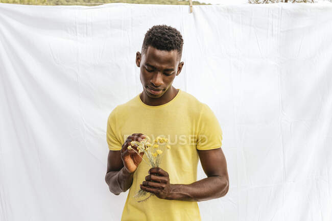 African American male with bouquet of yellow wildflowers looking down on white background — Stock Photo