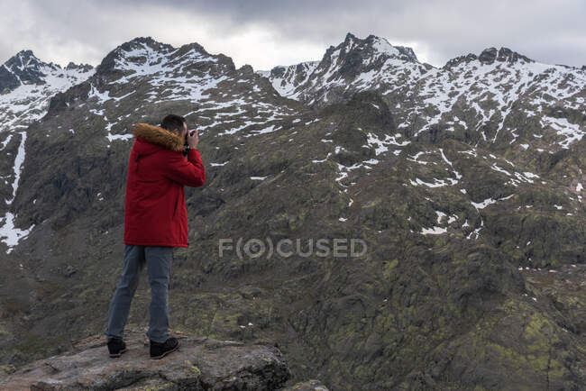 Full body man in outerwear shooting Sierra de Gredos mountain range covered with snow on cold day in Avila, Spain — Stock Photo