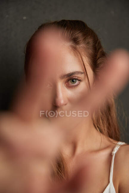 Joven hembra tierna extendiendo la mano hacia la cámara sobre fondo gris en el estudio - foto de stock