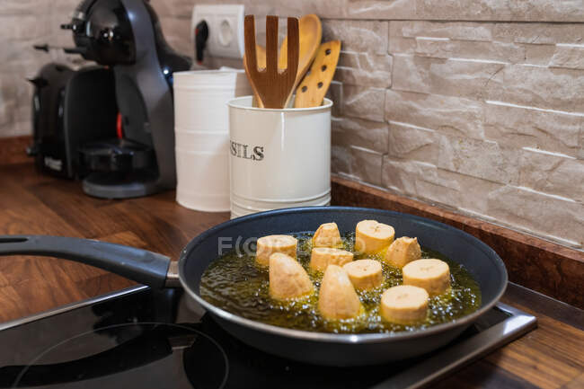 Кусочки плантацій обсмажуються в сковороді з олійкою для бульбашок на пічці проти асортованих спатул на кухні з кам 