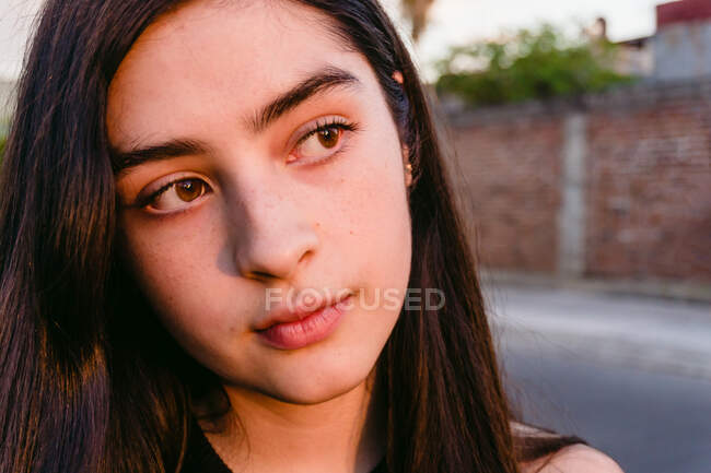 Portrait de jeune adolescente coûteuse aux longs cheveux bruns regardant la caméra le jour ensoleillé — Photo de stock