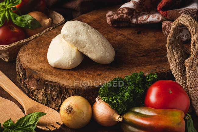 Balls of mozzarella cheese among various healthy products and organic spatulas with basil leaves on table — Stock Photo