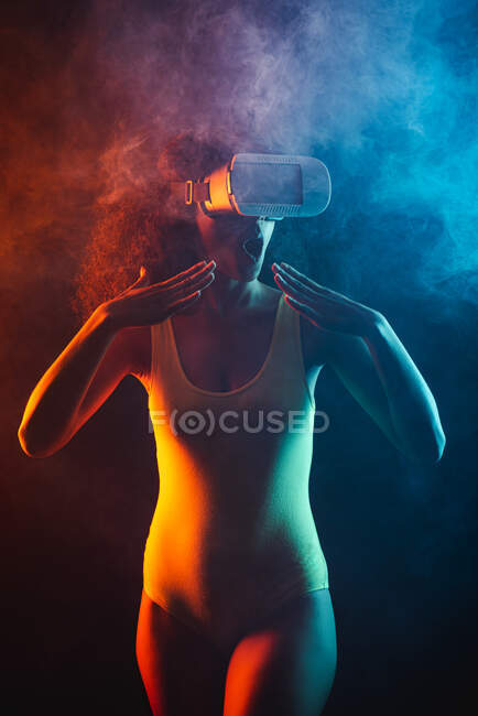 Anonyme ethnique étonnante femelle à bouche ouverte explorant la réalité virtuelle dans un casque sur fond noir — Photo de stock